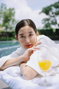 在游泳池附近的水疗床上，穿着白色浴袍的亚洲妇女的肖像。