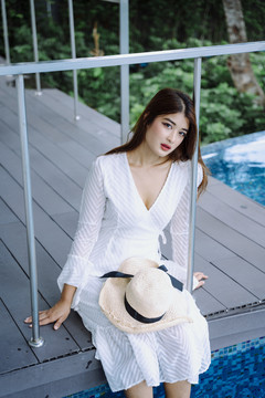 美丽的亚洲女游客坐在度假酒店的泳池边。