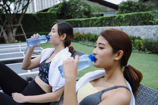 侧视图-美丽健康的女人一起从瓶子里喝水。