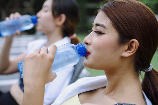 侧视图-美丽健康的女人一起从瓶子里喝水。