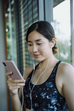 美丽健康的女人戴运动胸罩用耳机听音乐。她正在用智能手机选歌。