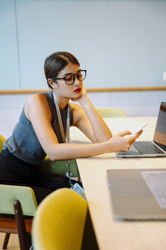 侧视图-亚洲女商人在办公室使用智能手机戴眼镜。