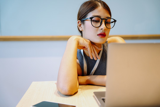 亚洲女商人戴着眼镜坐在笔记本电脑前。