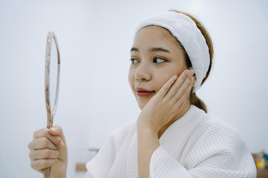 亚洲女性顾客在美容诊所接受面部水疗后看镜子。