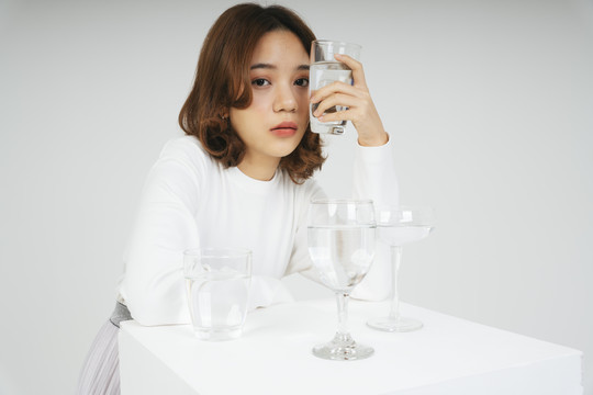 在白色背景上，亚洲女人戴着水杯在桌子上的时尚肖像。