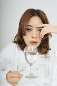 在白色背景上，亚洲女人戴着水杯在桌子上的时尚肖像。