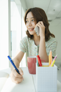 年轻的亚洲女人写书和打电话。