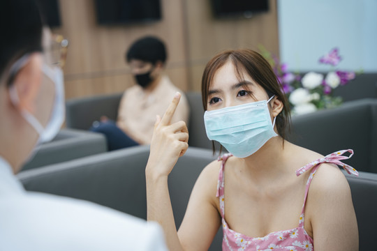 年轻的亚洲女人戴着面具在医院和医生交谈。
