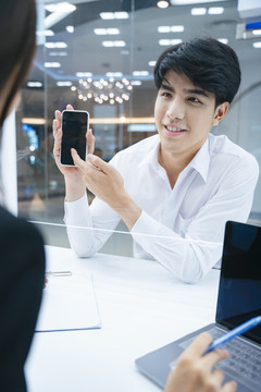 年轻的亚裔男子用智能手机向前台展示照片。
