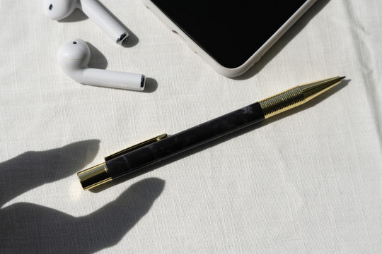 顶视图-商务办公桌，带金色钢笔、耳机和白色背景的智能手机。