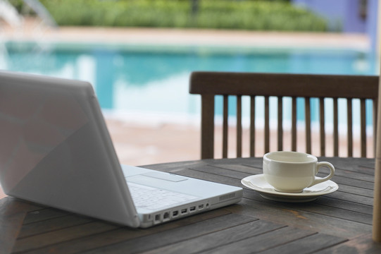 咖啡杯和笔记本电脑放在桌子上，可以看到游泳池的侧面。