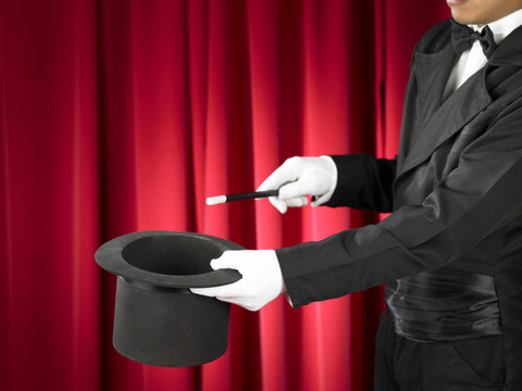 魔术师的手拿着魔杖和礼帽在舞台上。