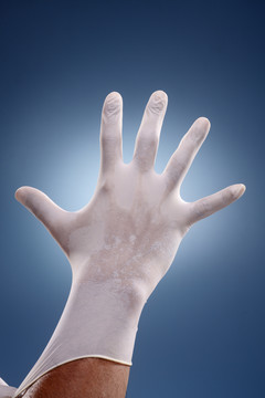 手戴上手术手套在一个创造性的蓝色背景。