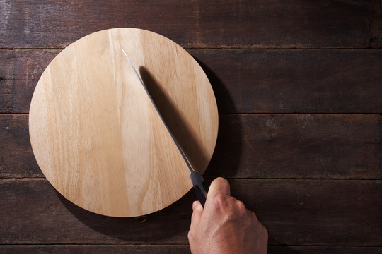 空的圆形木制切板，用于面包、比萨饼或牛排，刀放在厨房的桌子背景上，复制空间。俯视图，平面布置