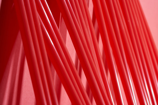 一排红色塑料吸管斜靠在红色背景的墙上