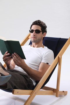 戴着太阳眼镜的人躺在躺椅上看书