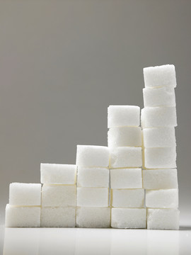 在灰色背景上上升的一堆方糖。这是一个由过量摄入糖引起的糖尿病或其他疾病的高风险概念