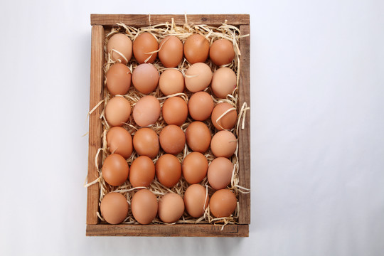 一堆新鲜的棕色鸡蛋和一些稻草放在木箱里