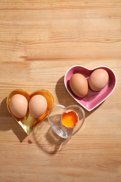 棕色鸡蛋，心形透明碗，木质背景。