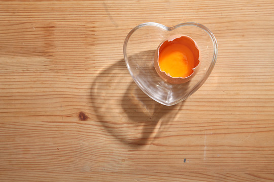 棕色鸡蛋，心形透明碗，木质背景。