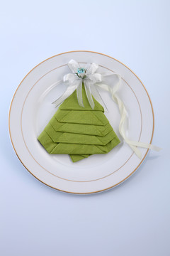 折叠成圣诞树形状的餐巾，盘子上有缎带