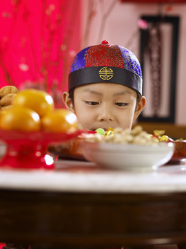 穿着传统服装的男孩在桌上偷看美味的食物