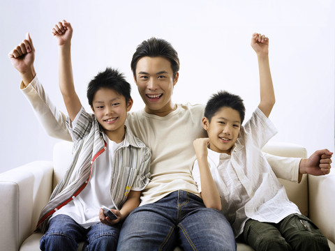 父亲和两个儿子在客厅边看电视边举手