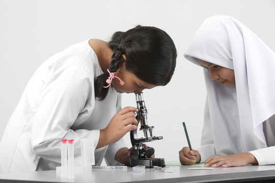 女学生在教室实验室里看显微镜