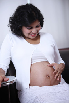 孕妇坐在沙发上，摸着肚子。