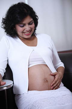 孕妇坐在沙发上，摸着肚子。