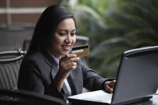 手持信用卡使用笔记本电脑的女人。