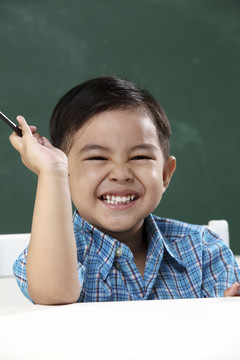 坐在教室里拿着铅笔的马来男孩
