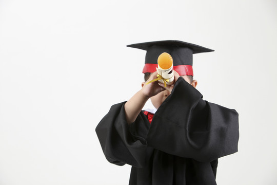 穿着毕业礼服拿着毕业证书的男孩的股票图像