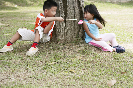 男孩和女孩靠在树干上，吃着棒棒糖