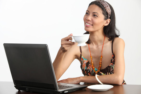 马来妇女拿着一个茶杯在笔记本电脑前
