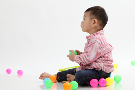 在白色背景上玩彩色球的中国男孩