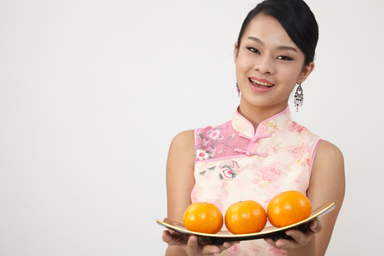 微笑的中国女人穿着传统旗袍拿着桔子盘