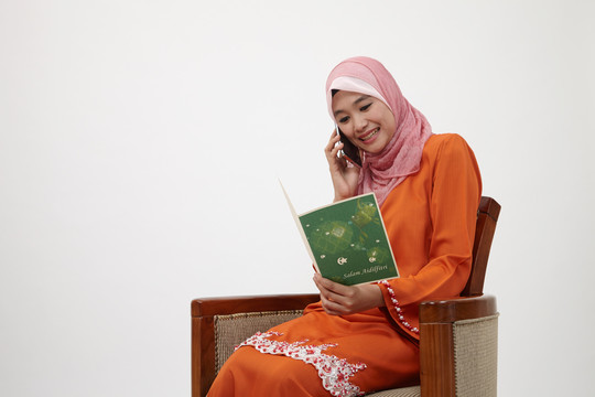 亚洲穆斯林马来妇女，图东手持瑞亚贺卡，用手机交谈