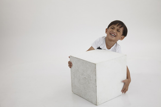 男孩试着举起一个沉重的白色盒子
