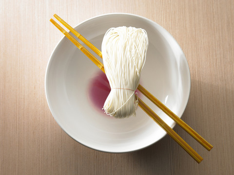 白碗上的一双红筷子，上面有面条