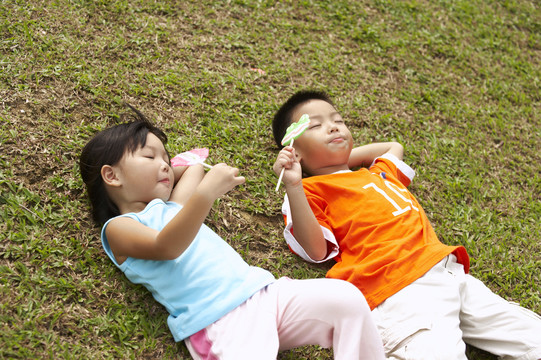 男孩和女孩躺在草地上，吃着棒棒糖