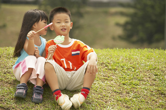 男孩和女孩坐在草地上，吃棒棒糖