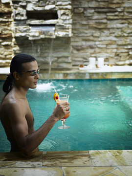 男子在泳池边喝鸡尾酒的资料照片