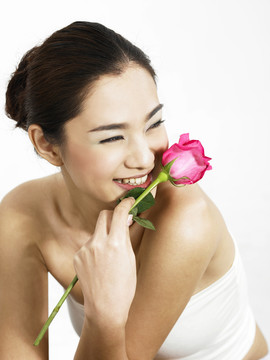 腰部向上的一张照片，一个女人拿着一朵粉红色的玫瑰，望着别处
