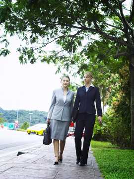 两位商务女士肩并肩走在人行道上