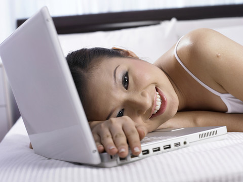 快乐的女孩躺在床上的电脑上，微笑着