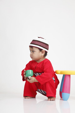 马来男孩身穿红色传统布匹，巴珠美拉育与佩利塔玩耍