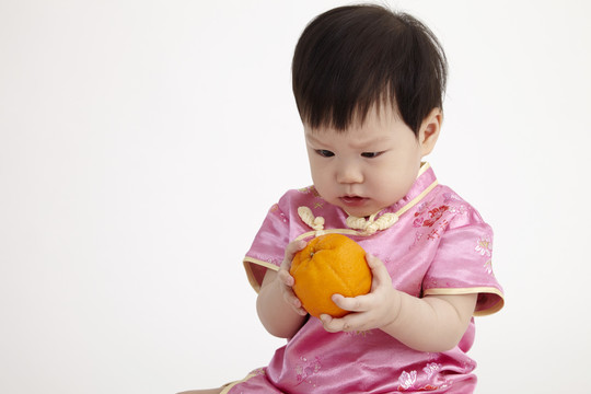 一个中国婴儿穿着雪松，手里拿着桔子