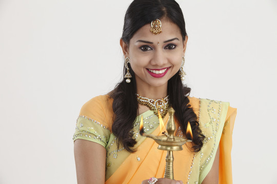 身着传统莎丽裙的印度年轻漂亮女子手持排灯节油灯，隔离在白色背景上。