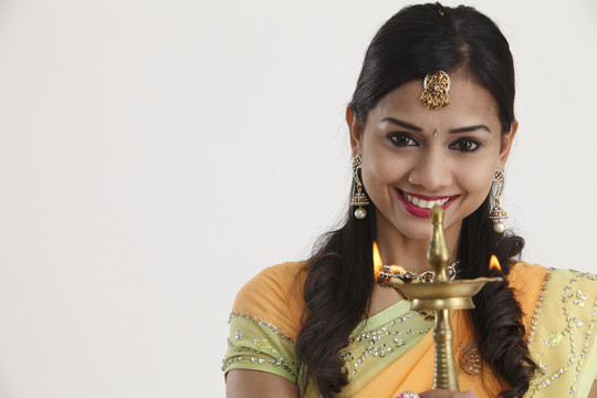 身着传统莎丽裙的印度年轻漂亮女子手持排灯节油灯，隔离在白色背景上。